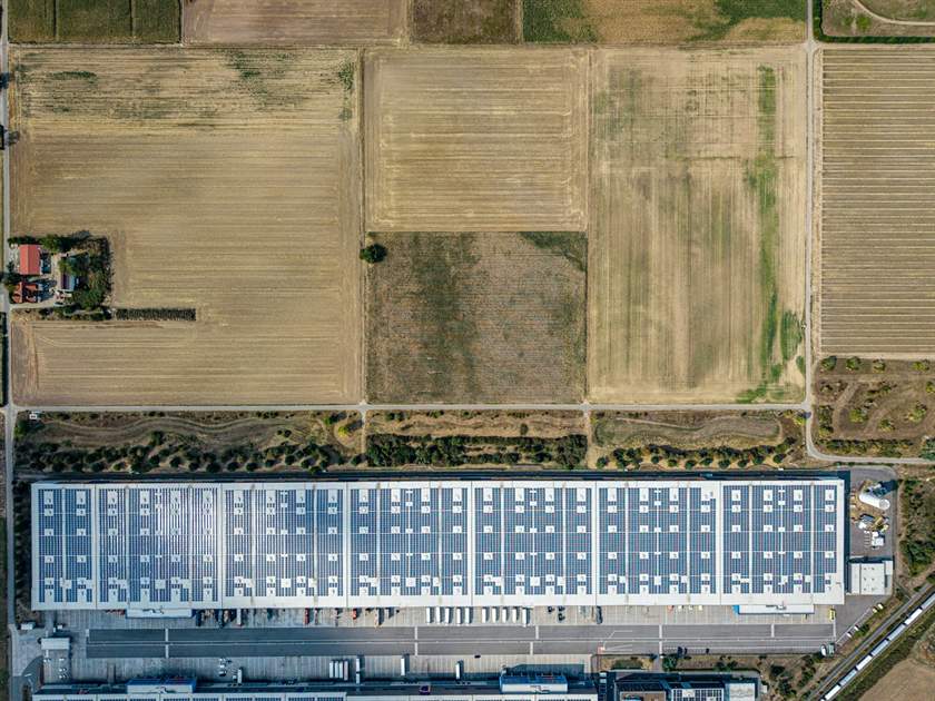 Vista aérea de galpão com telhado coberto por painéis solares ao lado de lavouras